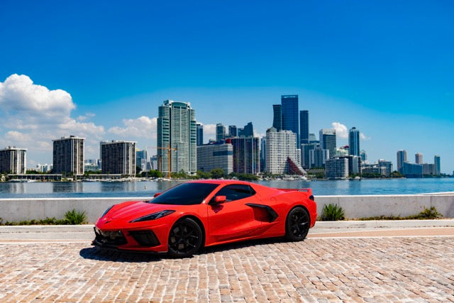 Red sports car parked on a brick road with a city skyline in the background