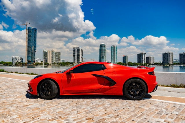 Red sports car on a waterfront road with city skyline in the background