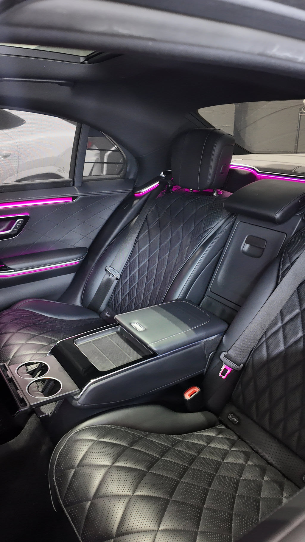 Luxury car interior with quilted black leather seats and pink ambient lighting.