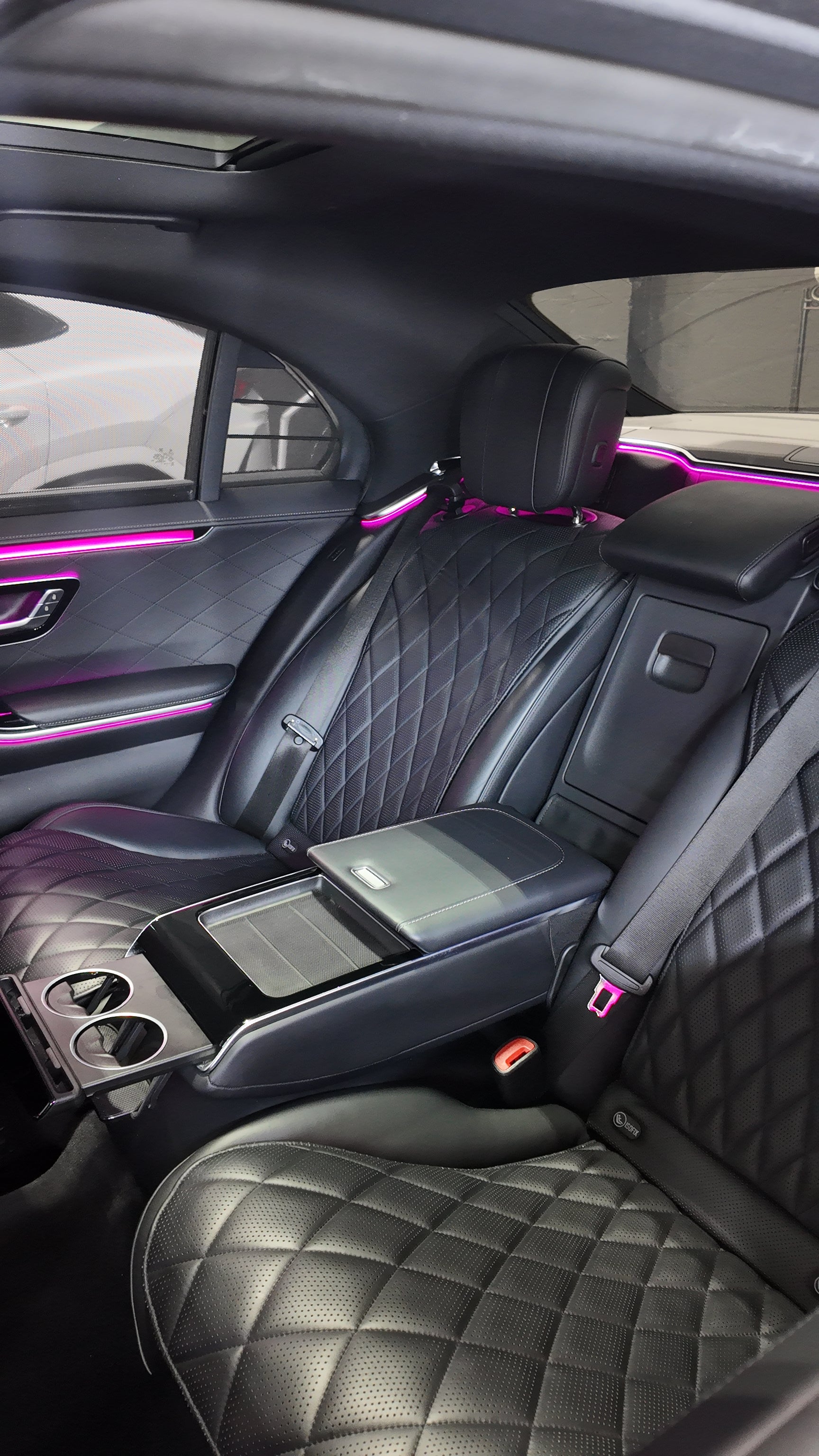 Luxury car interior with quilted black leather seats and pink ambient lighting.