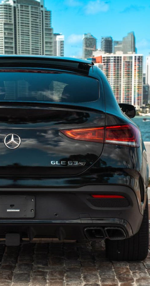 Black Mercedes-Benz car parked on a cobblestone street with a city skyline in the background
