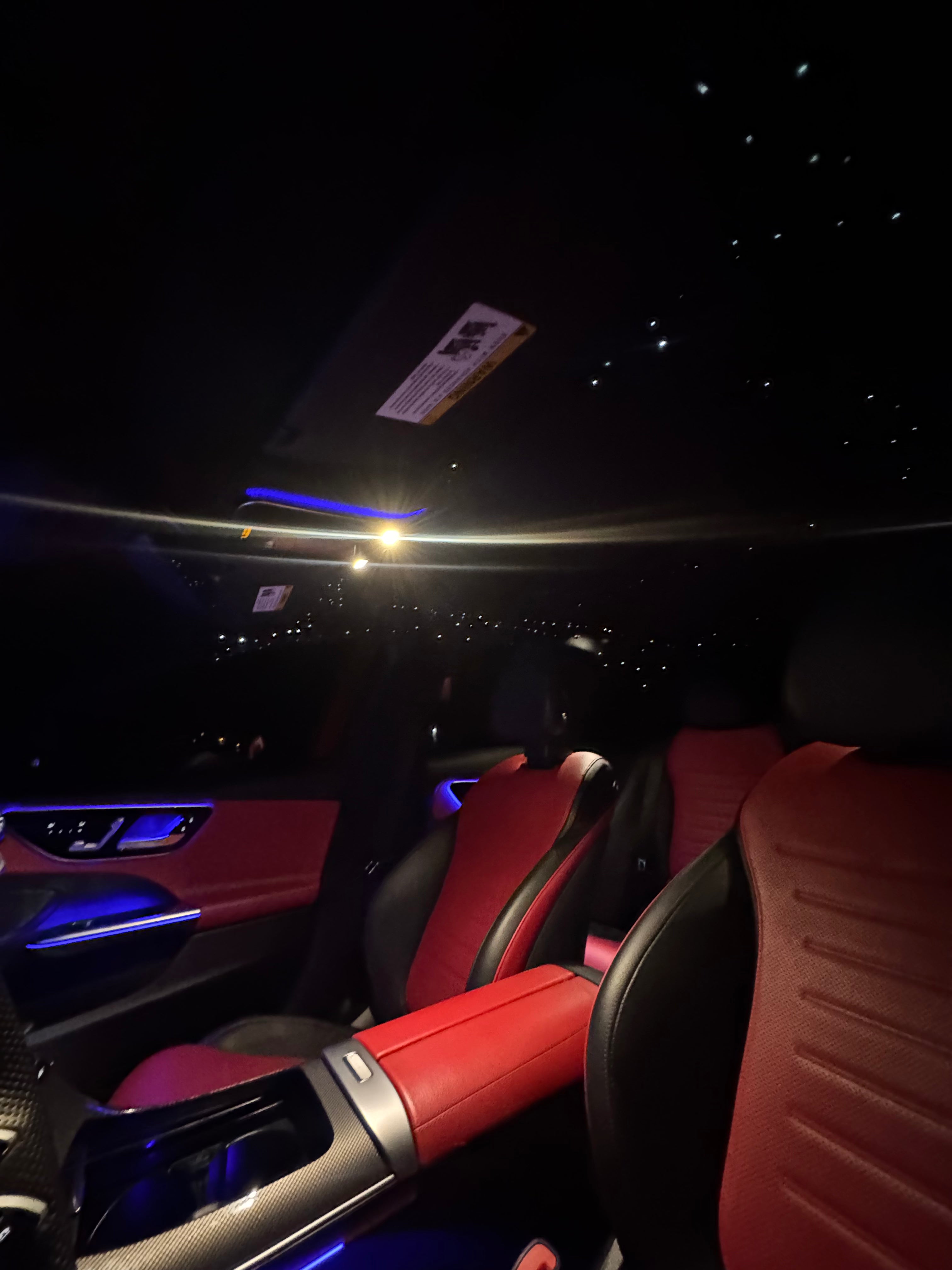 Car interior with red and black seats and a starry sky effect on the ceiling.