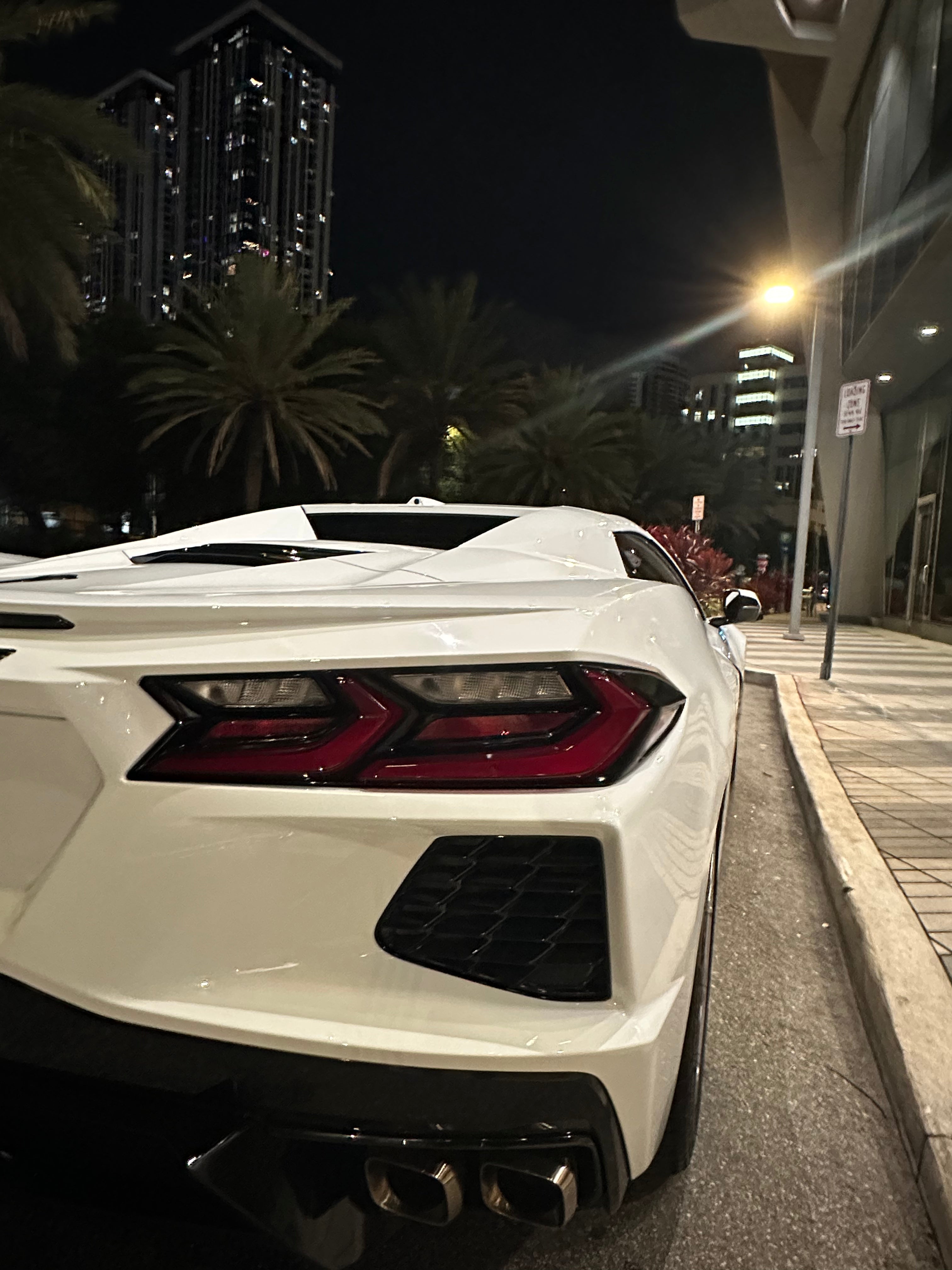 White sports car with red taillights parked on a street at night.