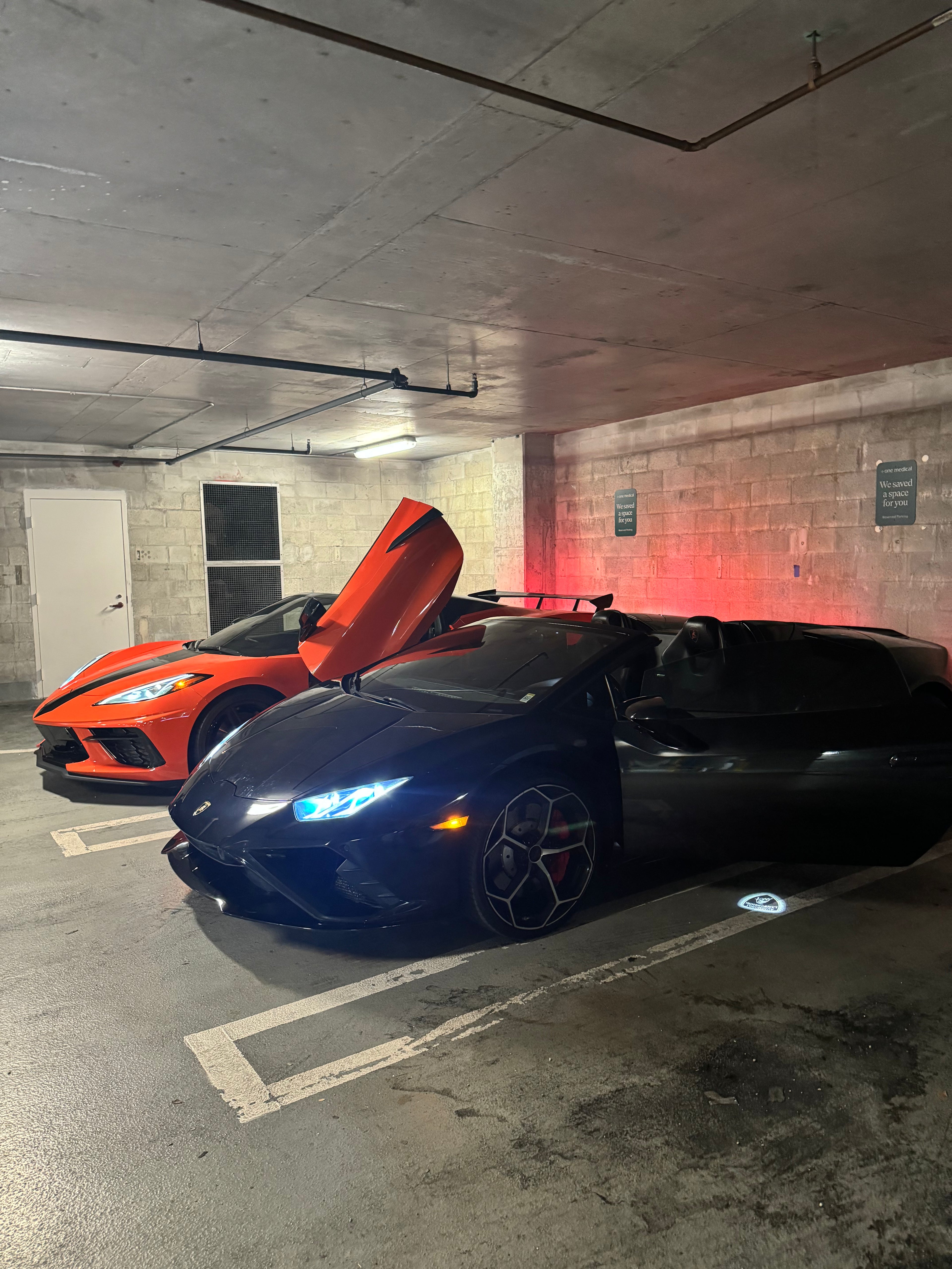 Two sports cars, one orange and one black, in a parking garage.
