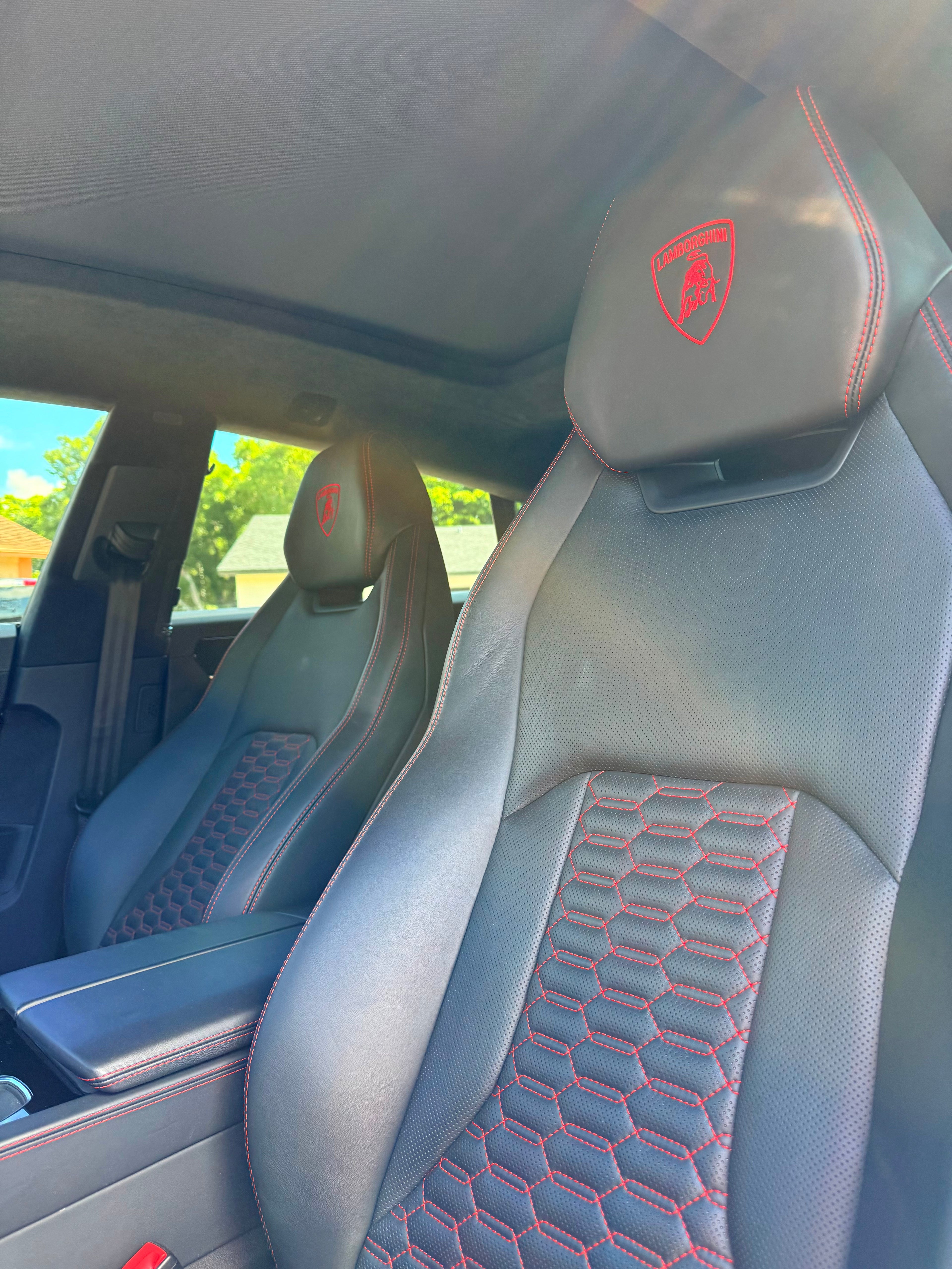 Car interior with black seats featuring a red Lamborghini logo on the headrest.