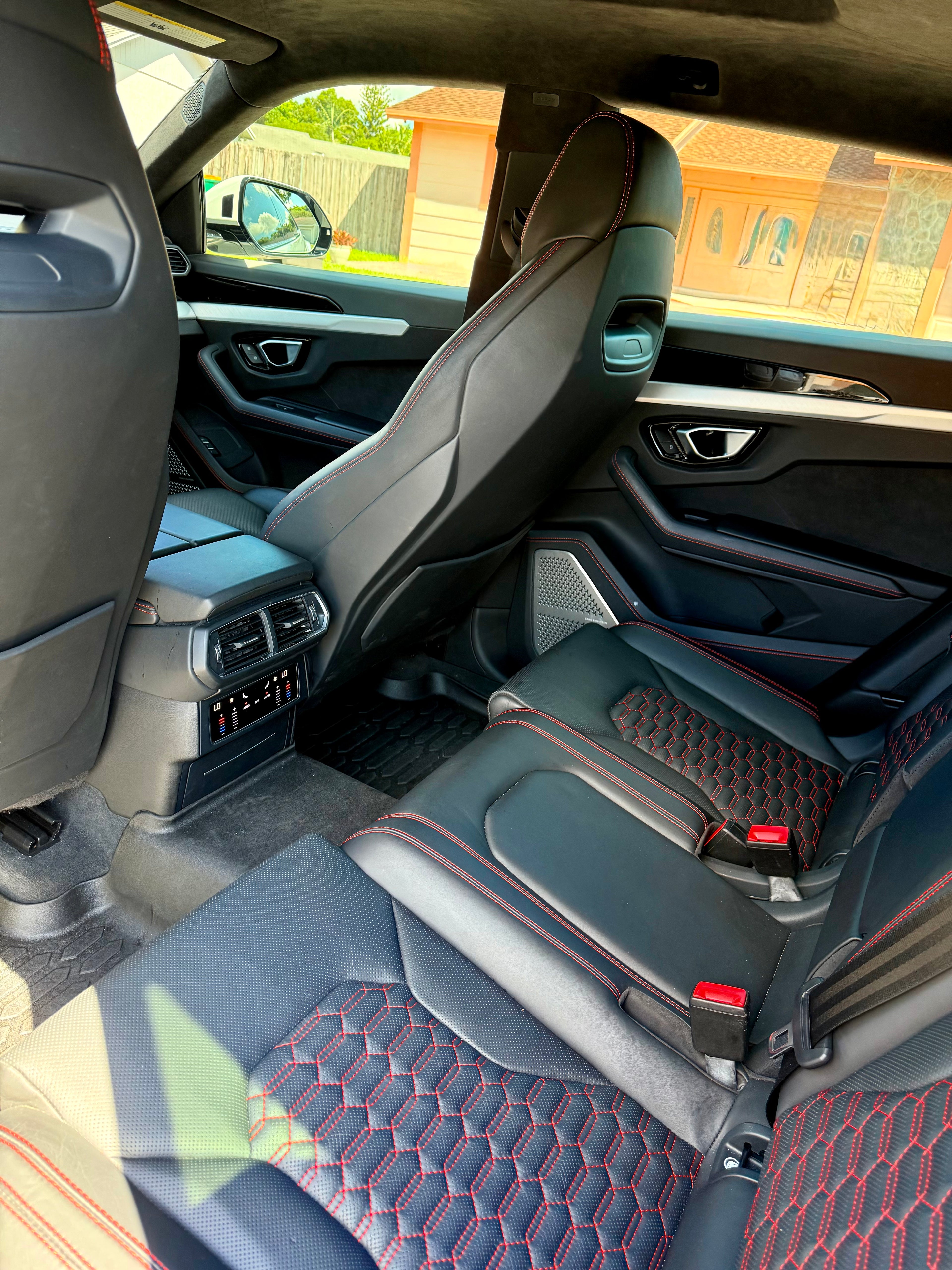 Car interior with black seats and red stitching, showing dashboard and side view mirror.