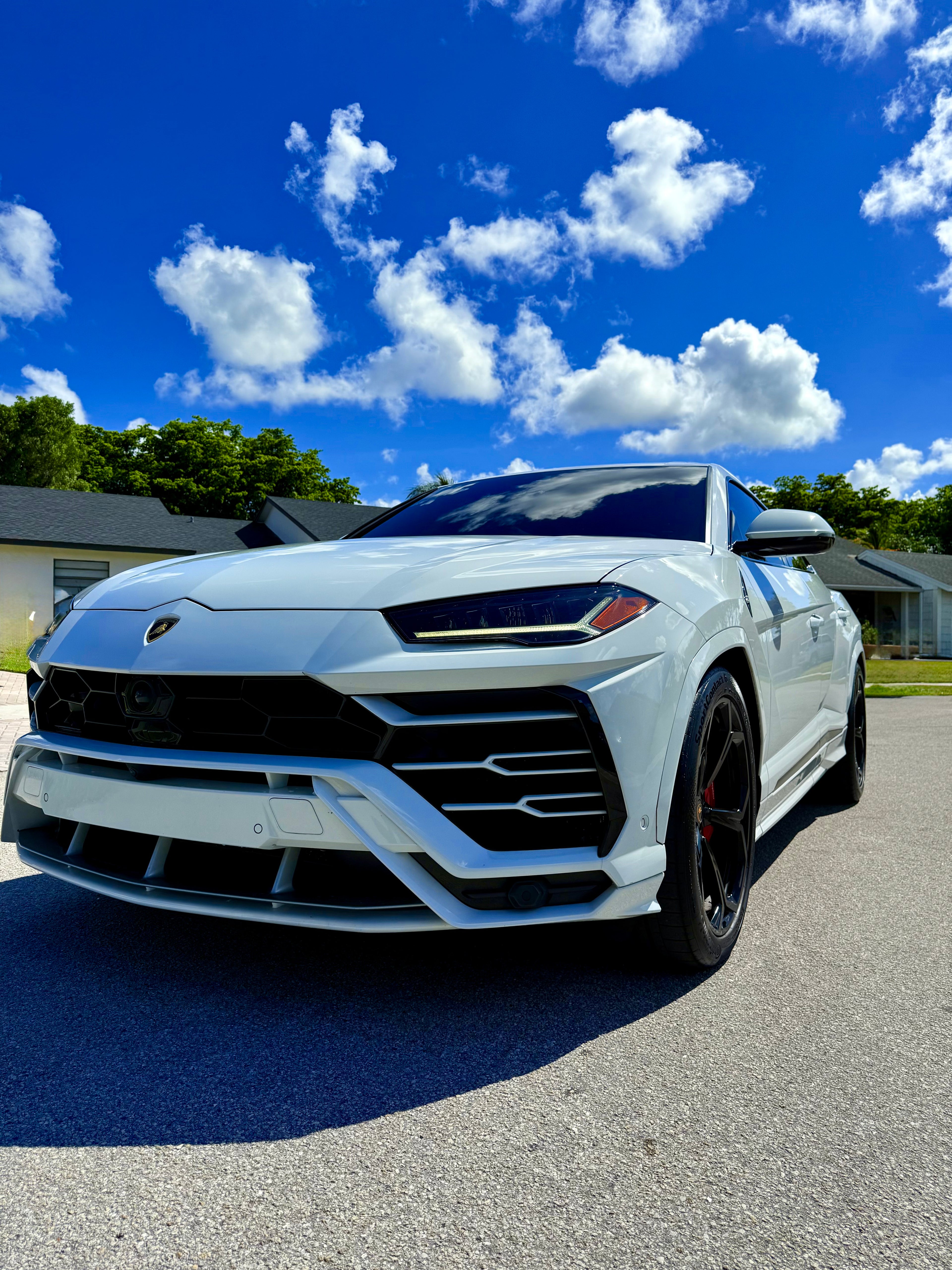 White Lamborghini Urus with a distinctive front grille on a sunny day.
