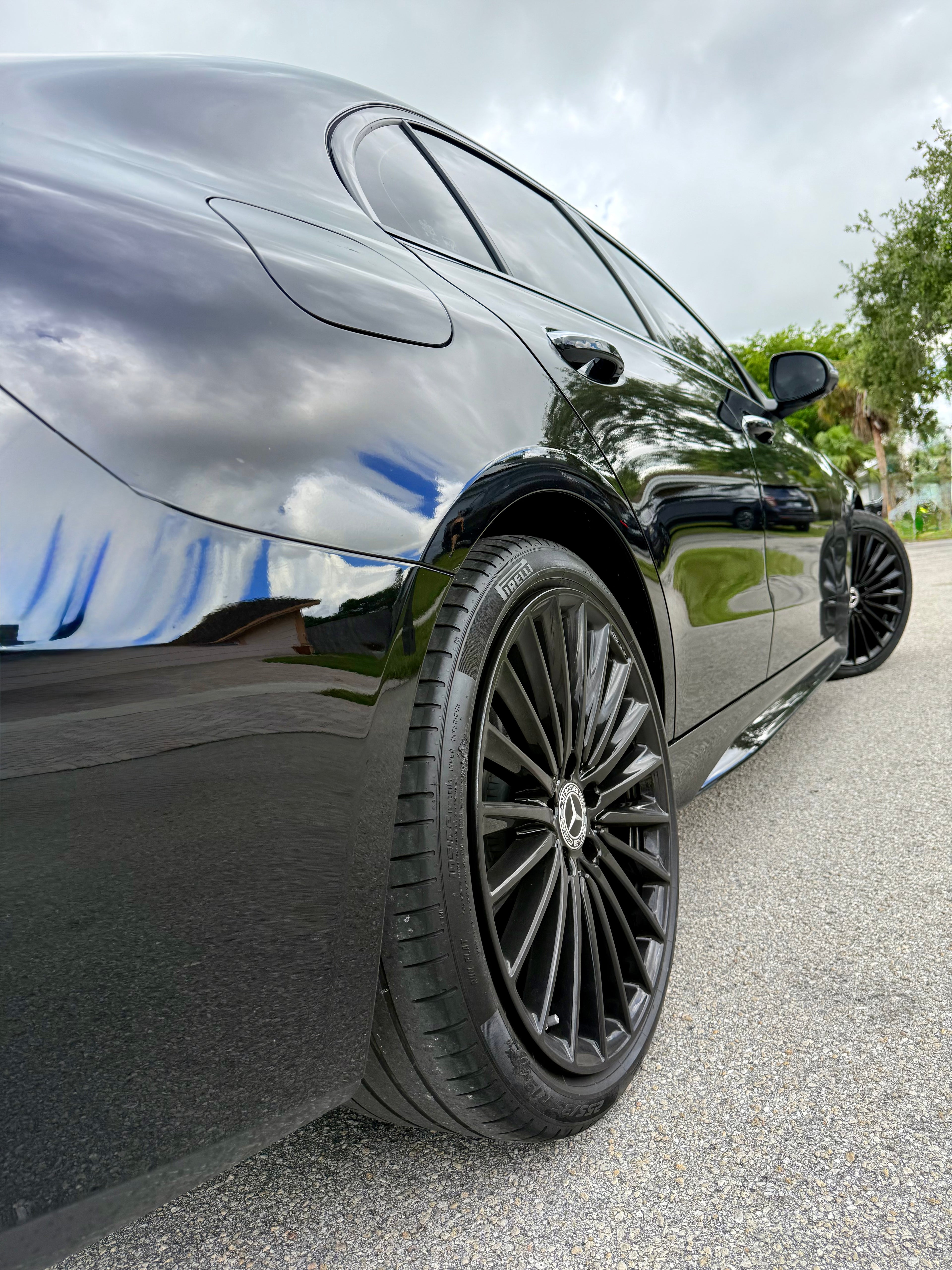 Close-up of a black car's wheel on a road with a cloudy sky.