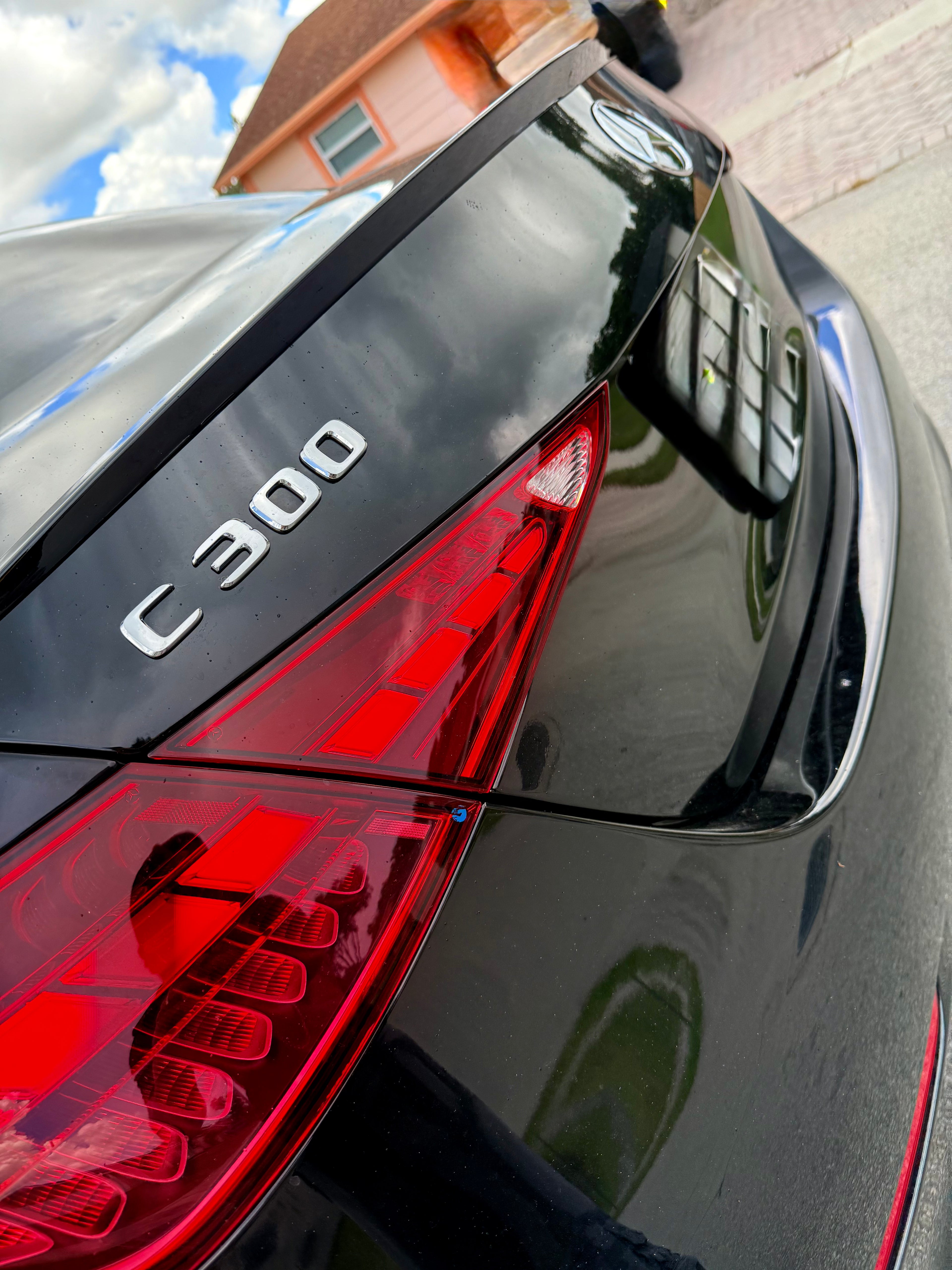 Close-up of a car's rear end with 'C300' badge, red taillights, and reflection on the glossy surface.