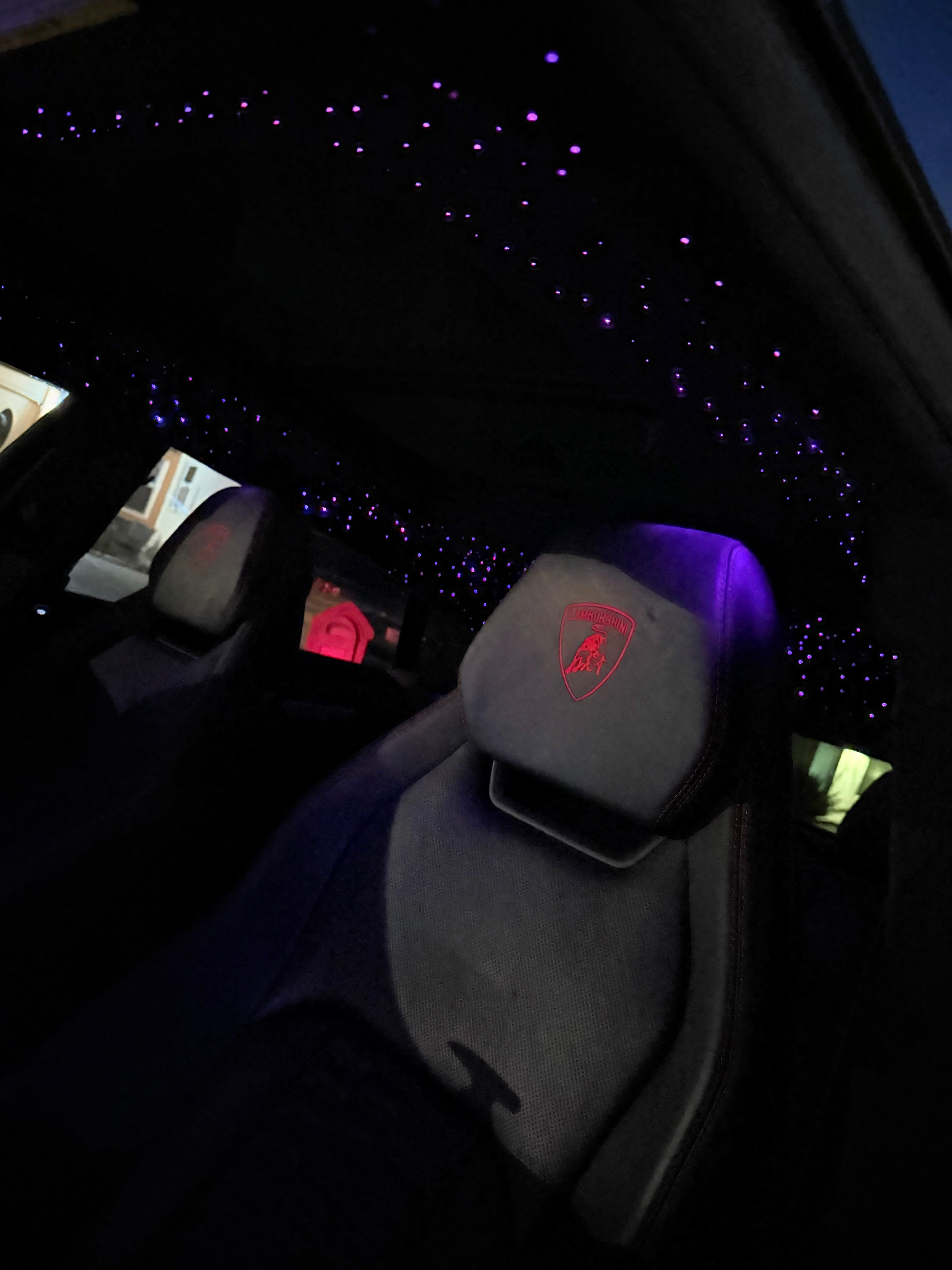 Car interior with illuminated dashboard and steering wheel Lamborghini emblem.