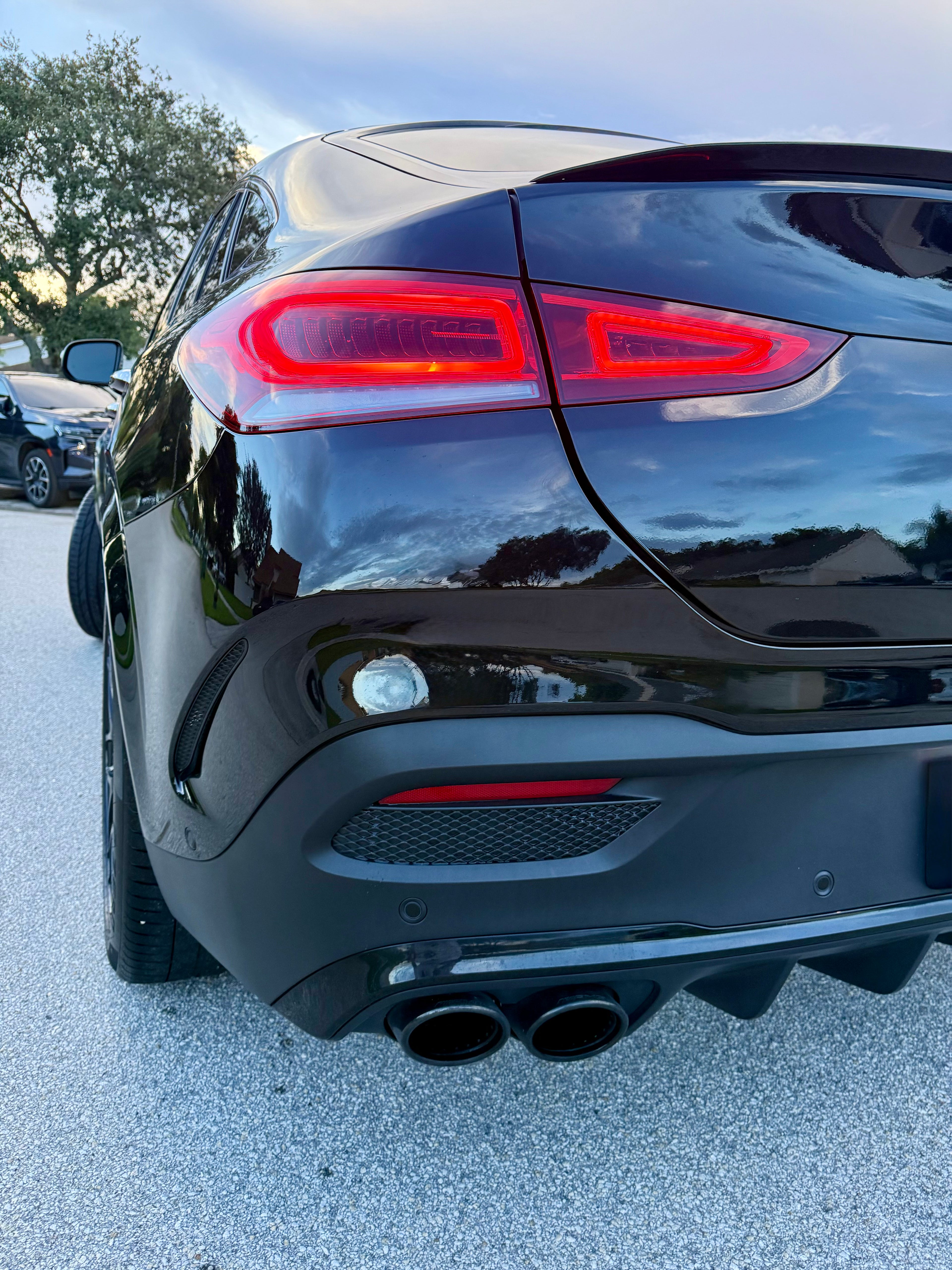 Black car's rear end with red taillights on a light gray pavement.