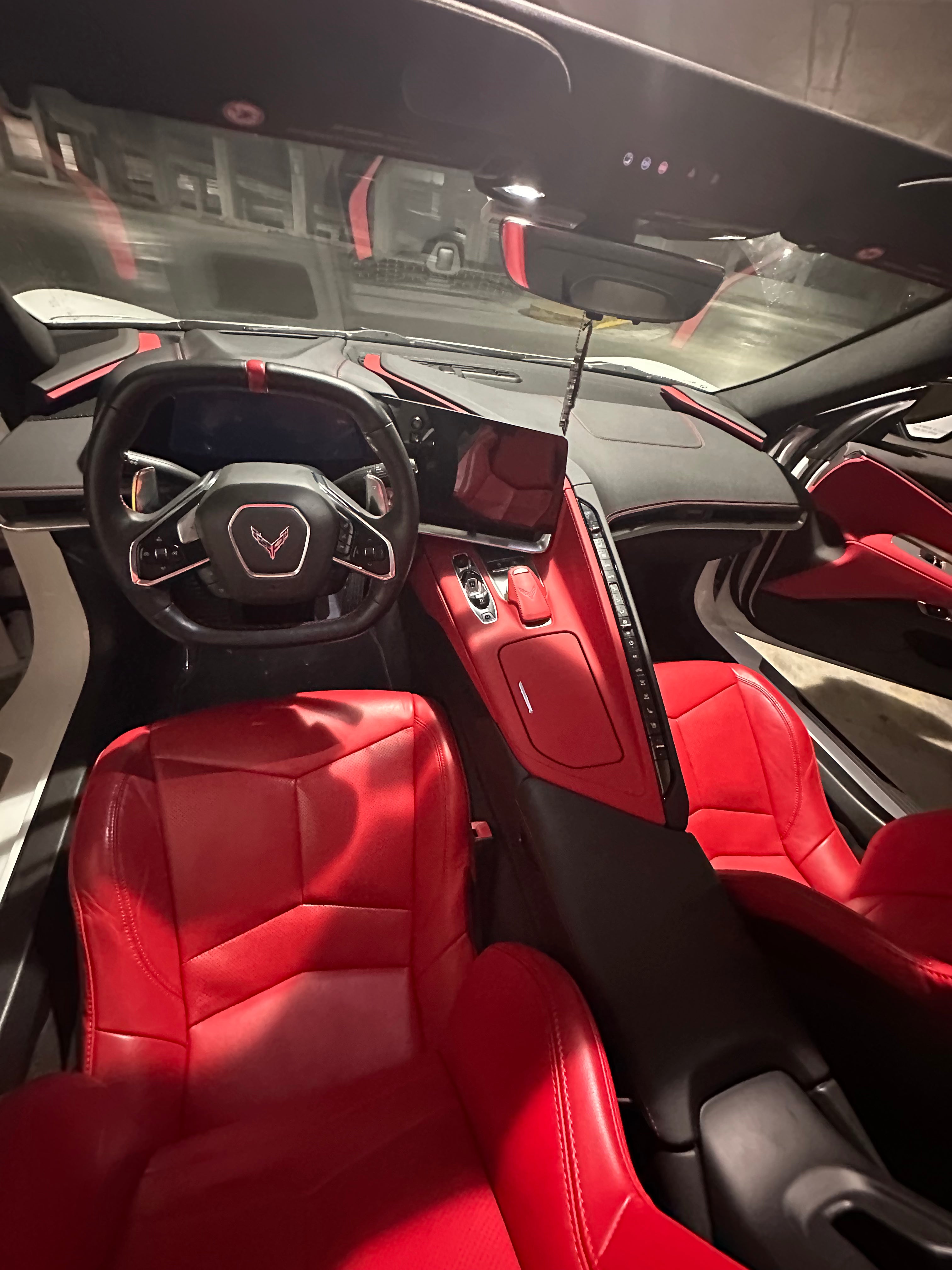 Car interior with red seats and dashboard, featuring a steering wheel and door panels.