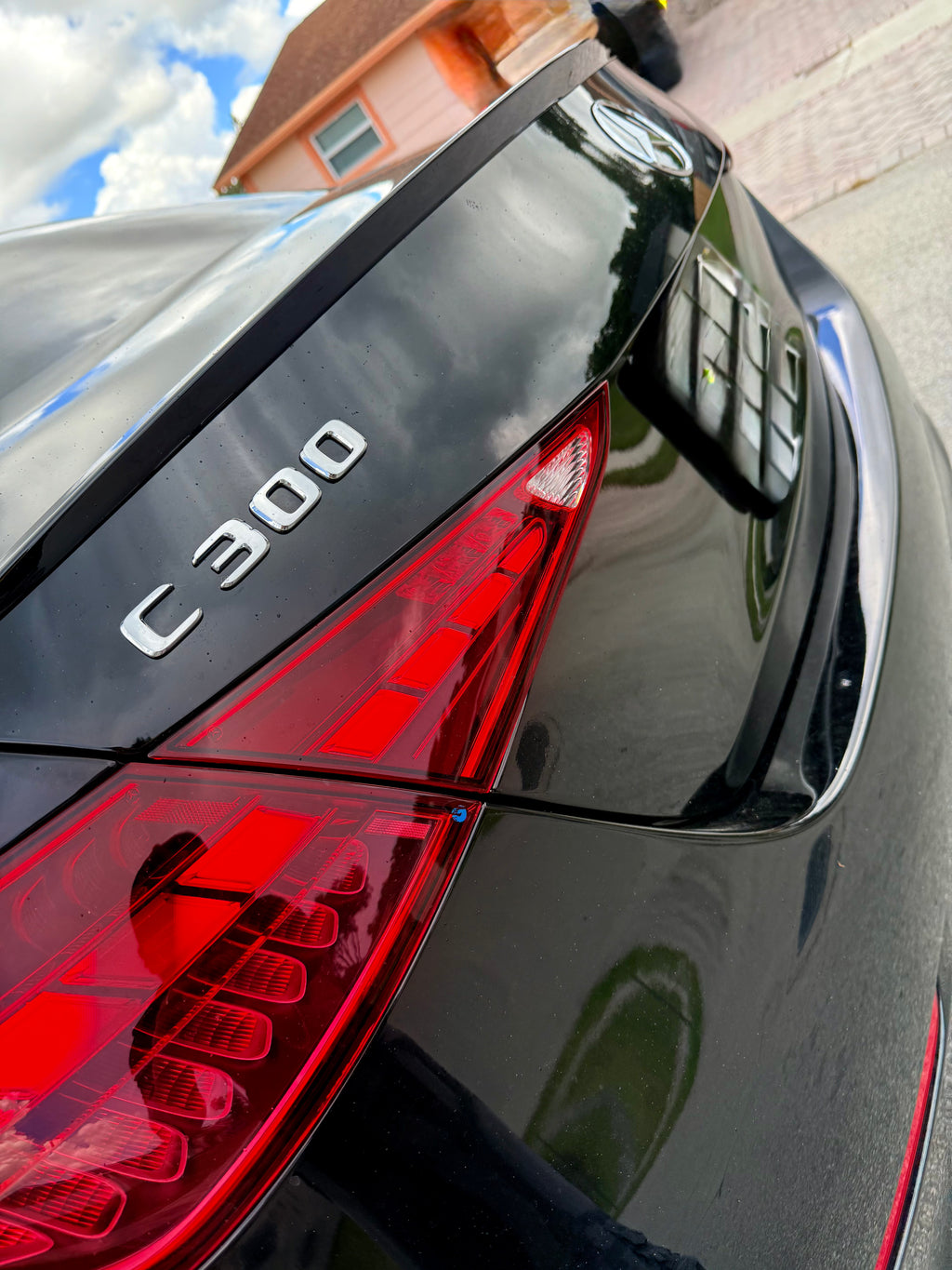 Close-up of a car's rear end with 'C300' badge, red taillights, and reflection on the glossy surface.