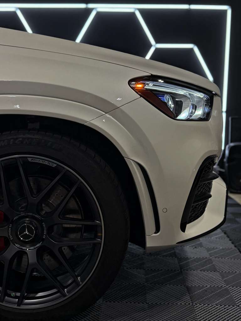 Close-up of a car's headlight and front wheel with a geometric light pattern in the background.