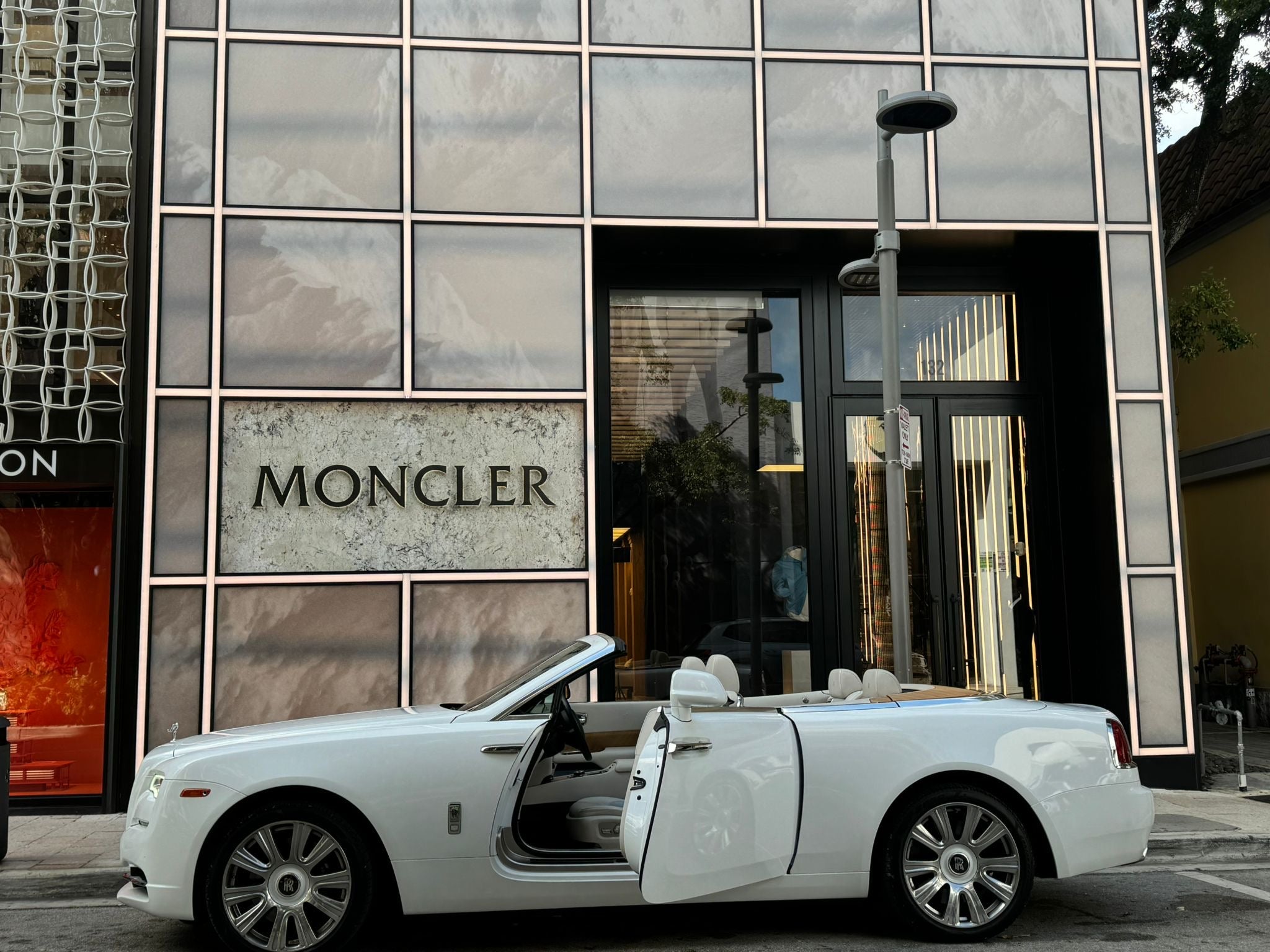 White convertible car with open door in front of a Moncler store