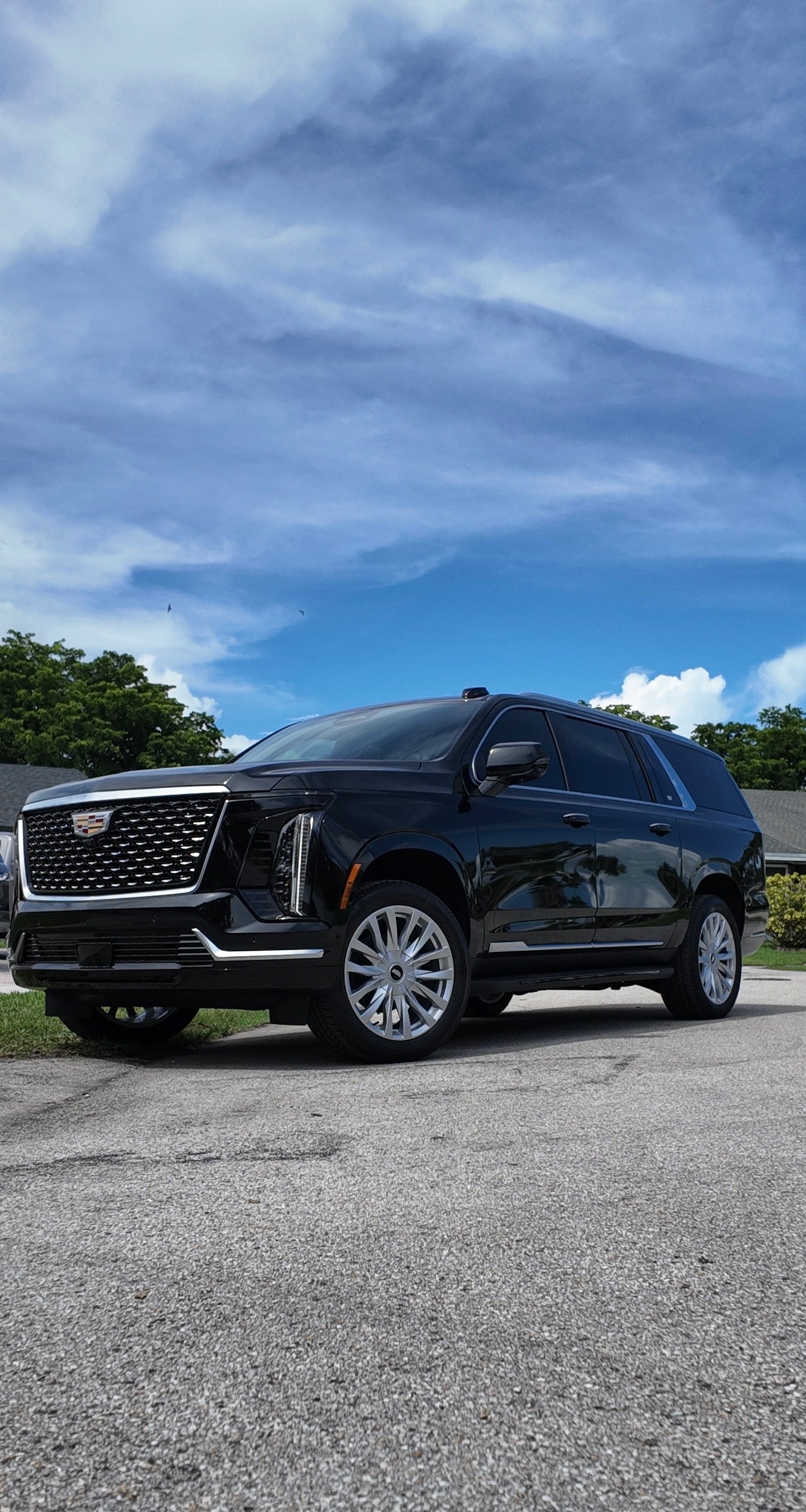 Black Cadillac SUV parked on a paved surface with a blue sky and clouds in the background.