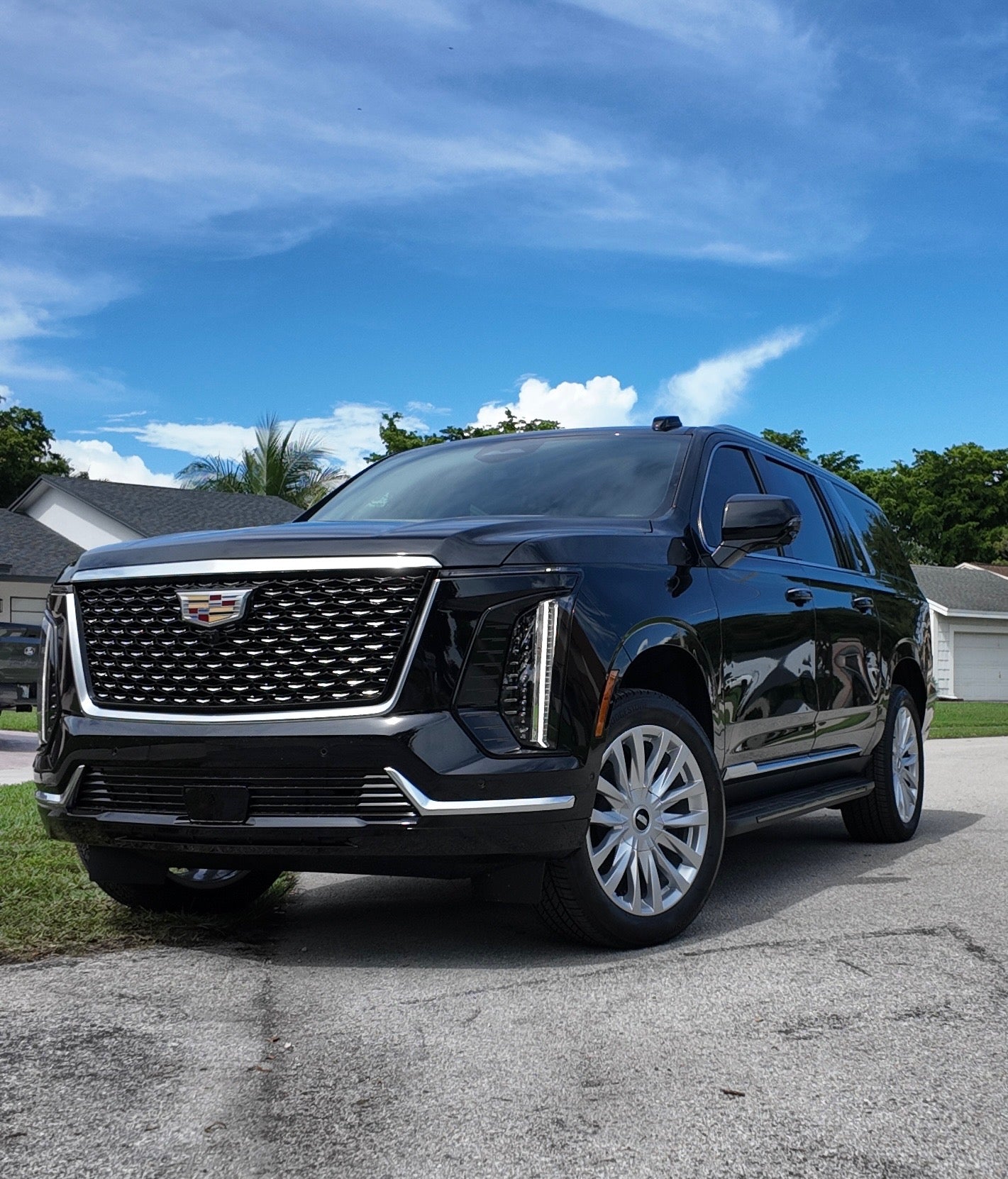 Black Cadillac SUV parked on a driveway with a blue sky and clouds in the background.